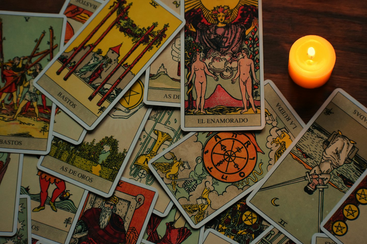 Colorful tarot cards laid out on dark wood next to a burning orange candle.